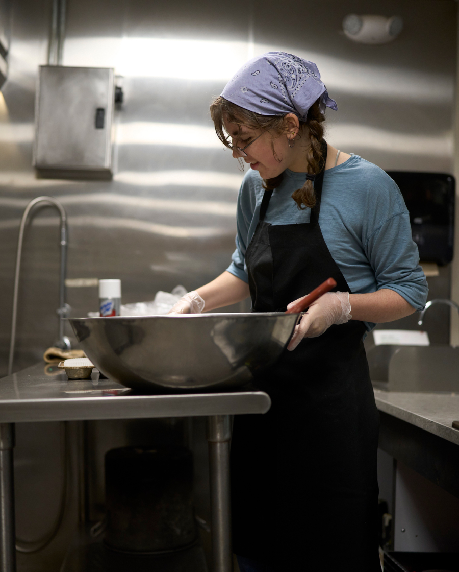 A dining crew student stands in a stainless steel kitchen preparing food