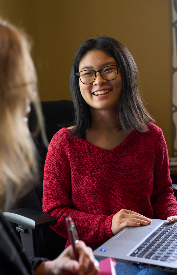 A student is turning their computer towards their advisor to show them what they've been working on with a smile.