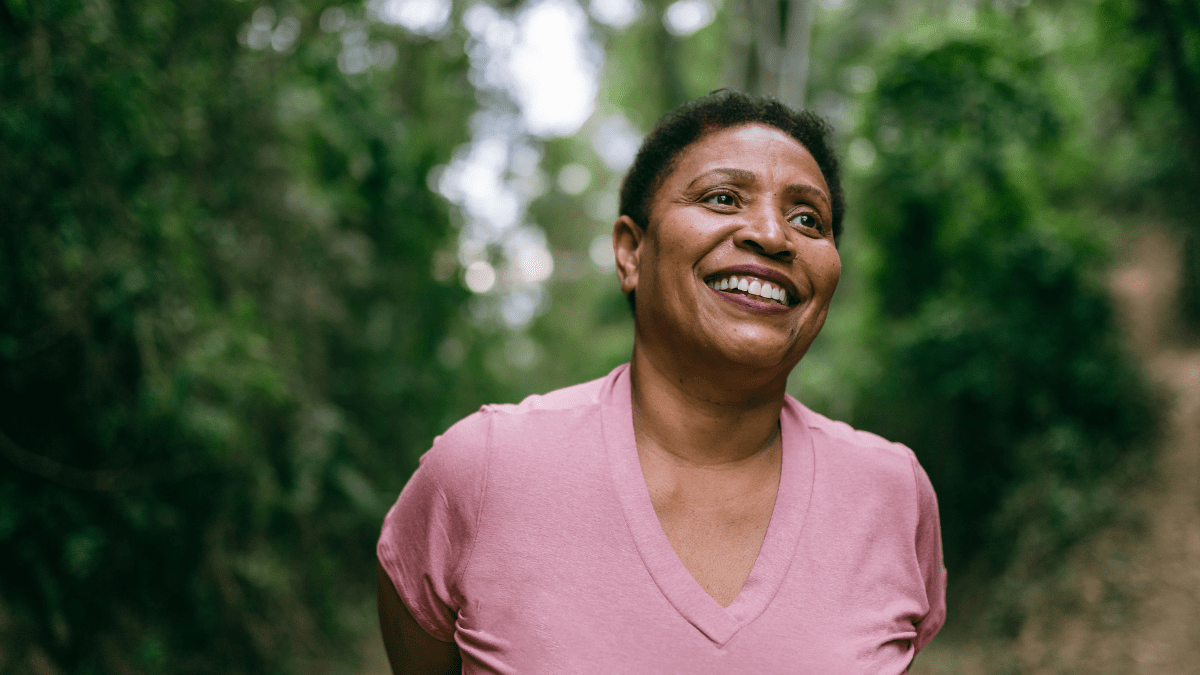 woman smiling outside among trees, enjoying the benefits of green spaces