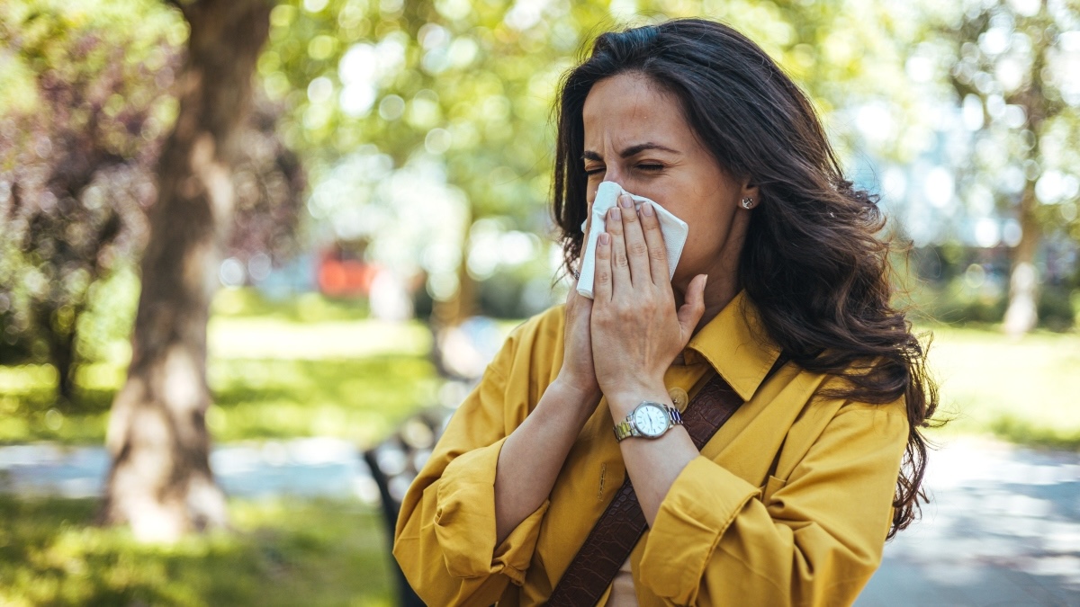 A woman outdoors sneezing due to fall allergies