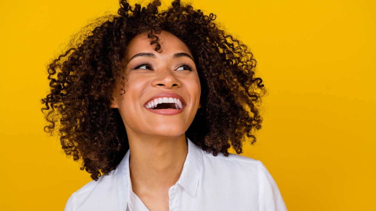 A woman laughing against a yellow background to improve her focus