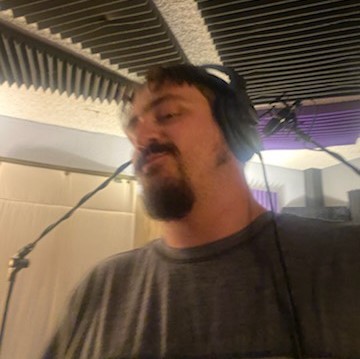 Casey Smith, giving the camera a chin-out smirk while wearing a drab green t-shirt. black hair and goatee