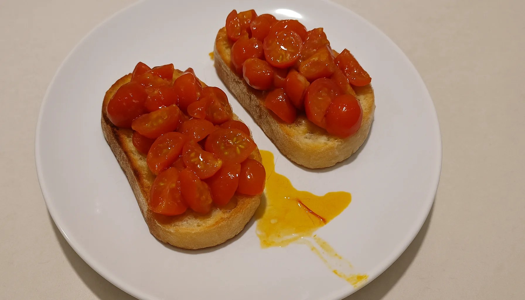 Bruschette con pomodorini e zafferano su pane tostato, in un piatto bianco su un piano cucina chiaro — ricetta Zafferù con zafferano in stimmi di Carrù (Piemonte)