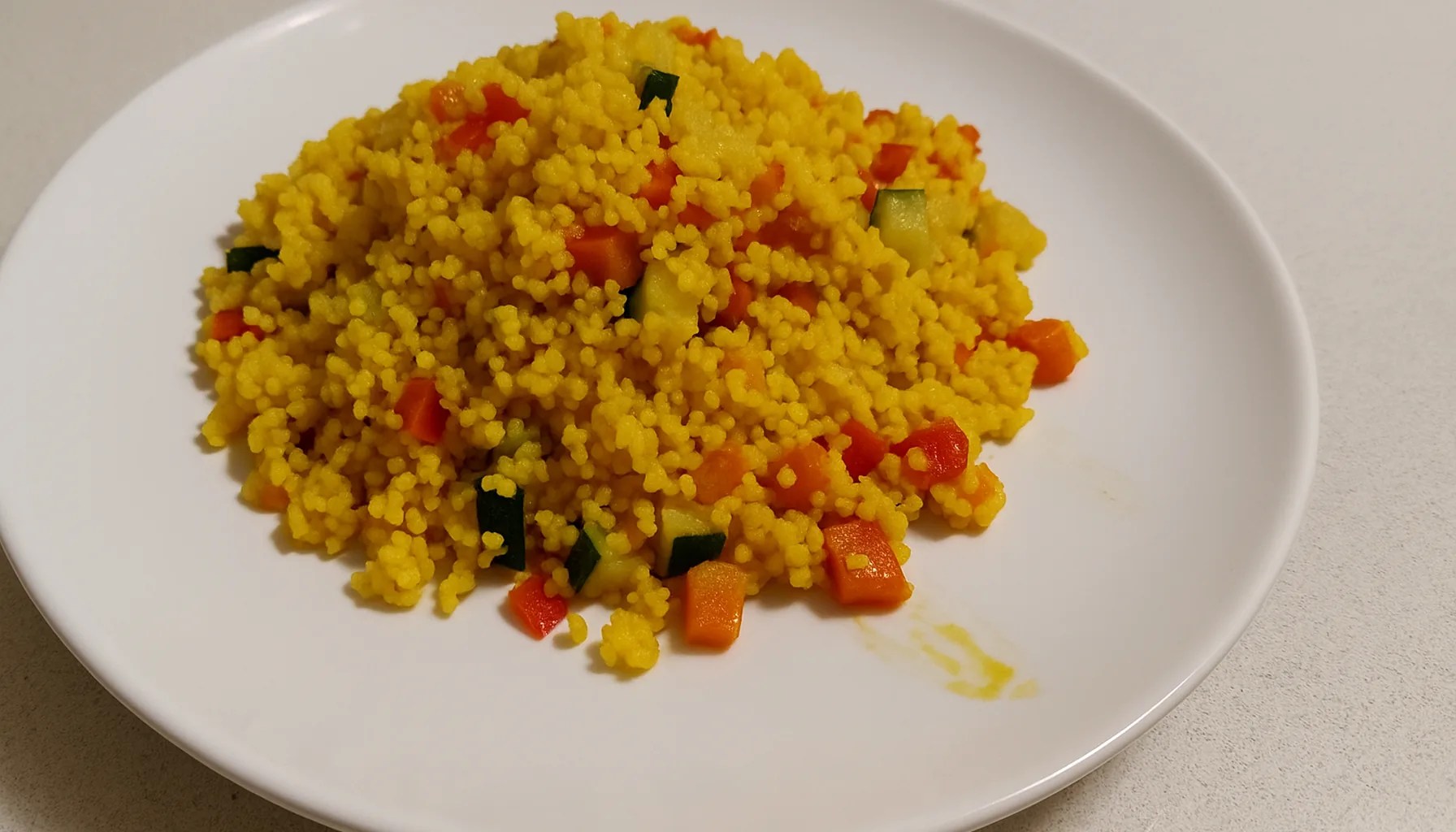 Couscous allo zafferano con verdure a cubetti, giallo e colorato, in un piatto bianco su un piano cucina chiaro — ricetta Zafferù con zafferano in stimmi di Carrù (Piemonte)