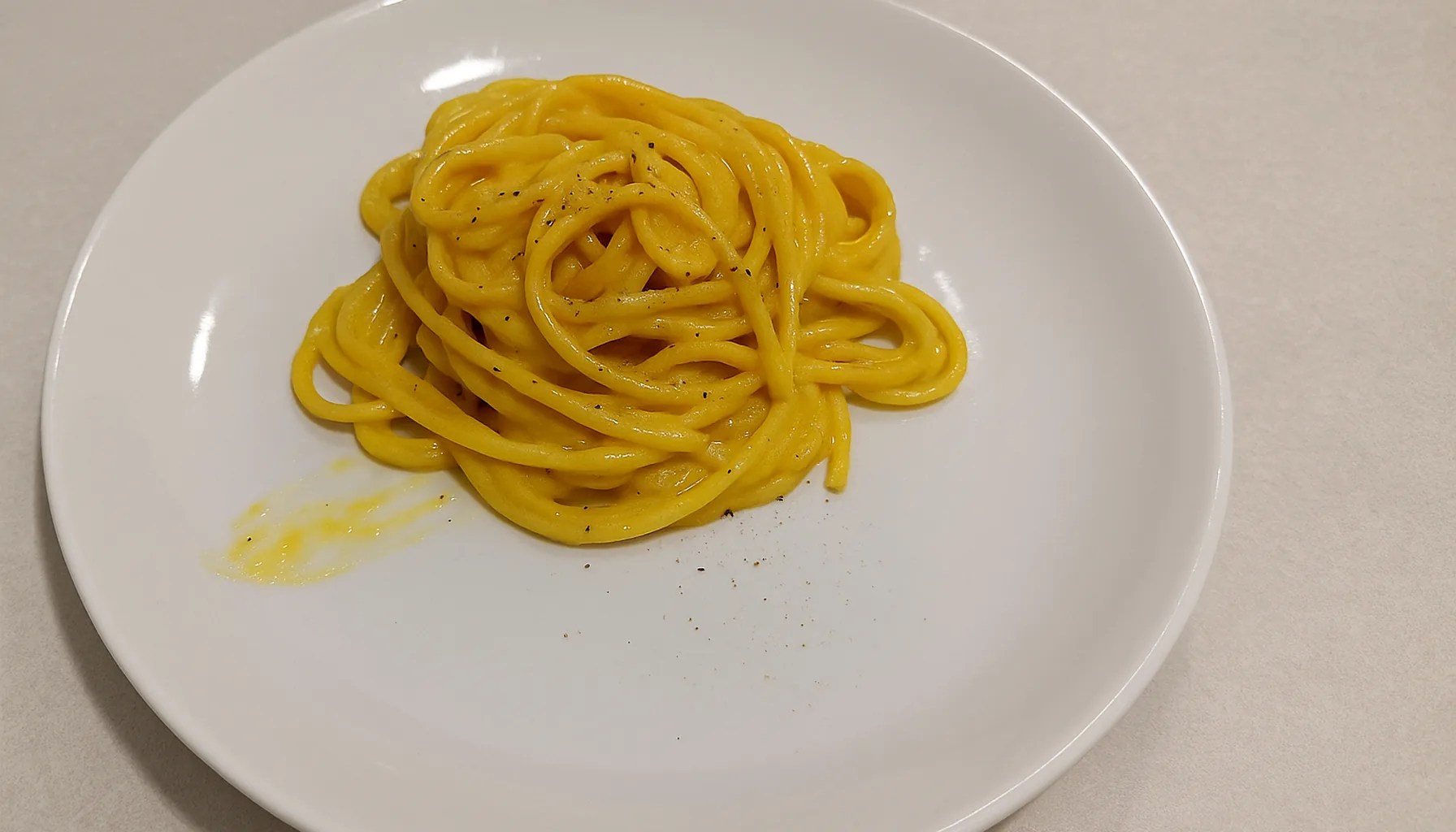 Pasta allo zafferano e cacio, cremosa e gialla, in un piatto bianco su un piano cucina chiaro — ricetta Zafferù con zafferano in stimmi di Carrù (Piemonte)