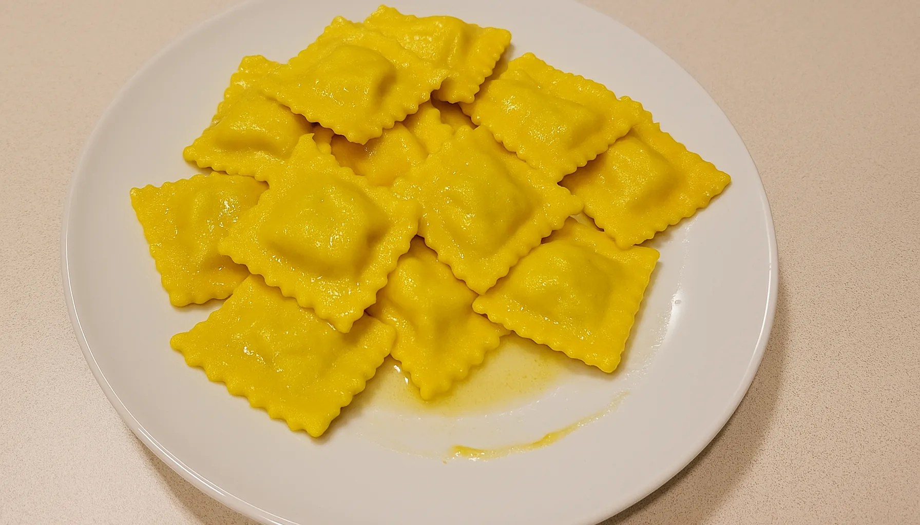 Ravioli allo zafferano e ricotta, gialli, conditi al burro, in un piatto bianco su un piano cucina chiaro — ricetta Zafferù con zafferano in stimmi di Carrù (Piemonte)