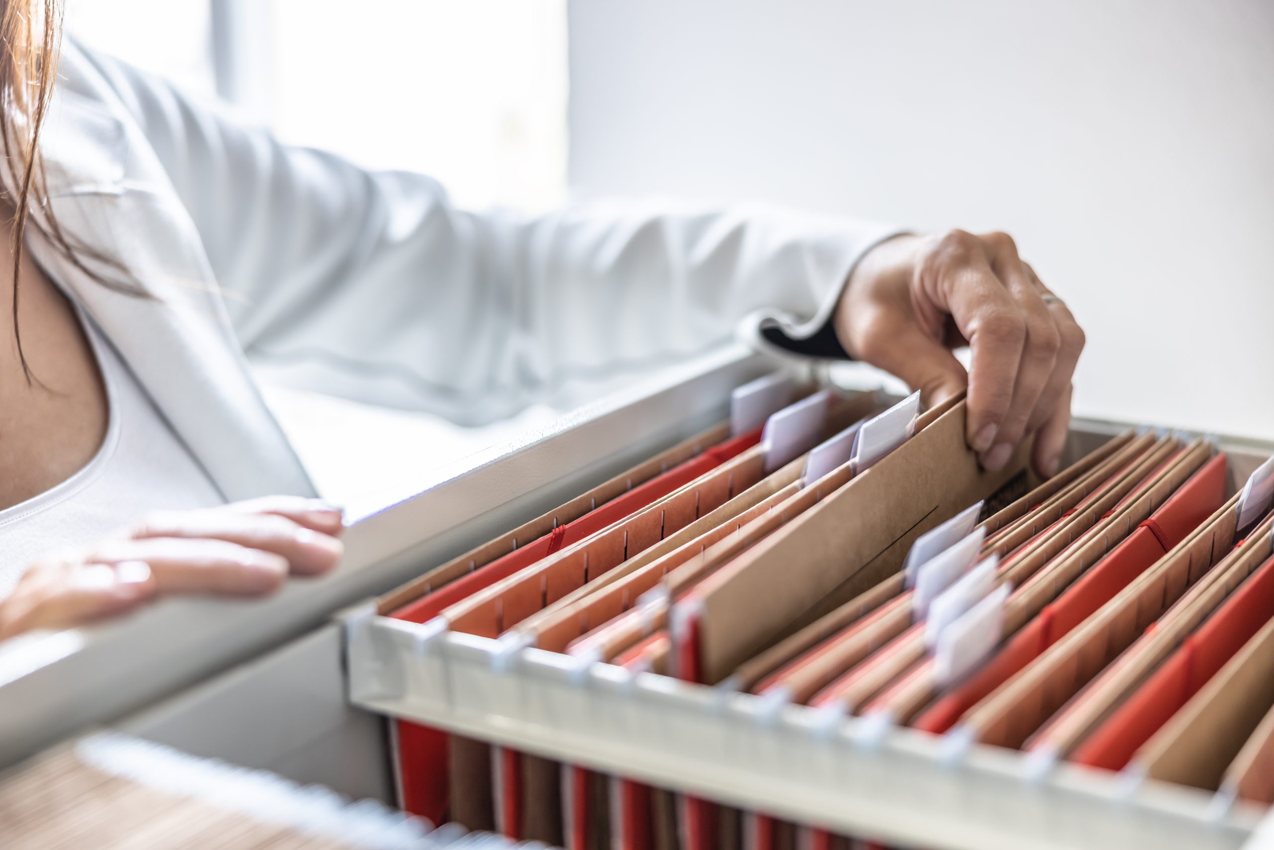 A person holds a folder taken from an open binder on a desk. The image illustrates the concept of organizing your contracts and the outdated practice of using physical contracts.