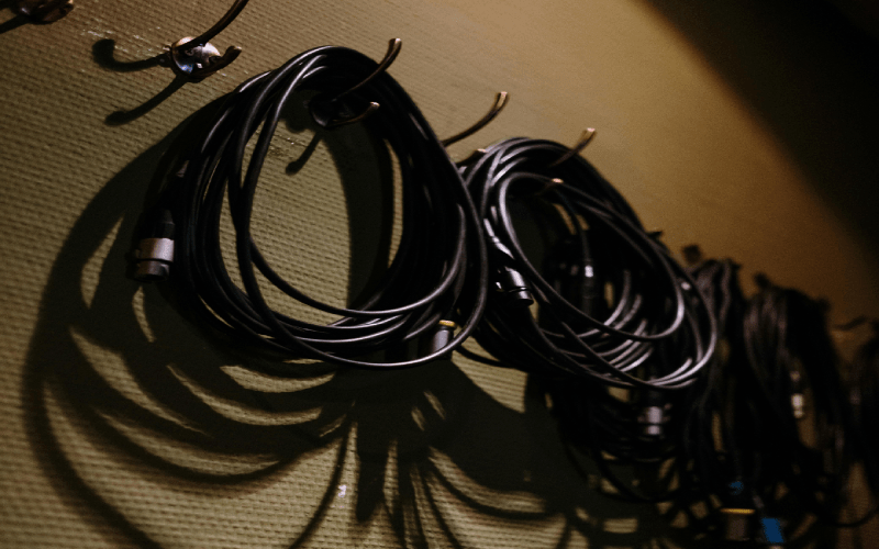 Coiled audio cables hanging on wall-mounted hooks against a textured, olive-green wall.