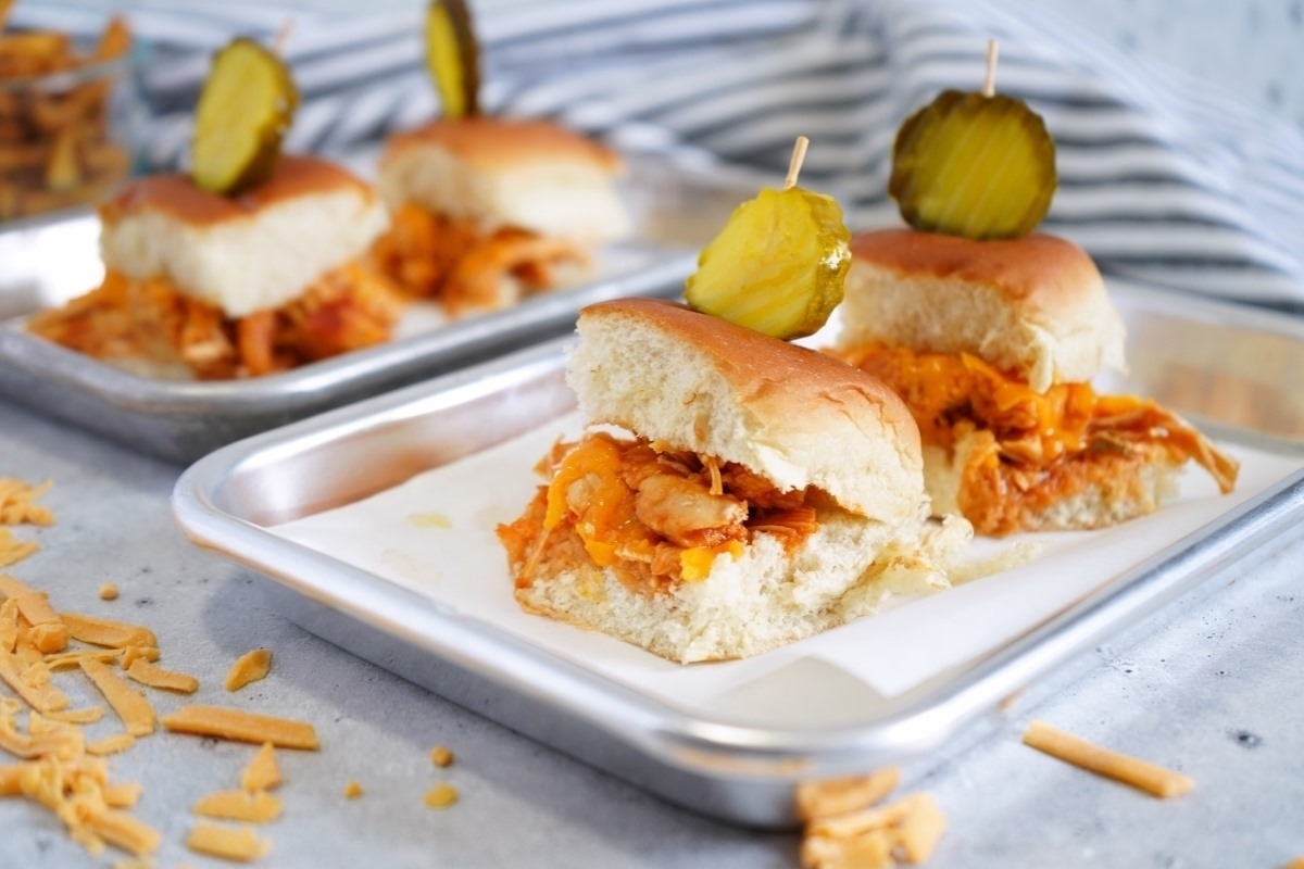 Delicious chicken sliders on a tray with pickles.