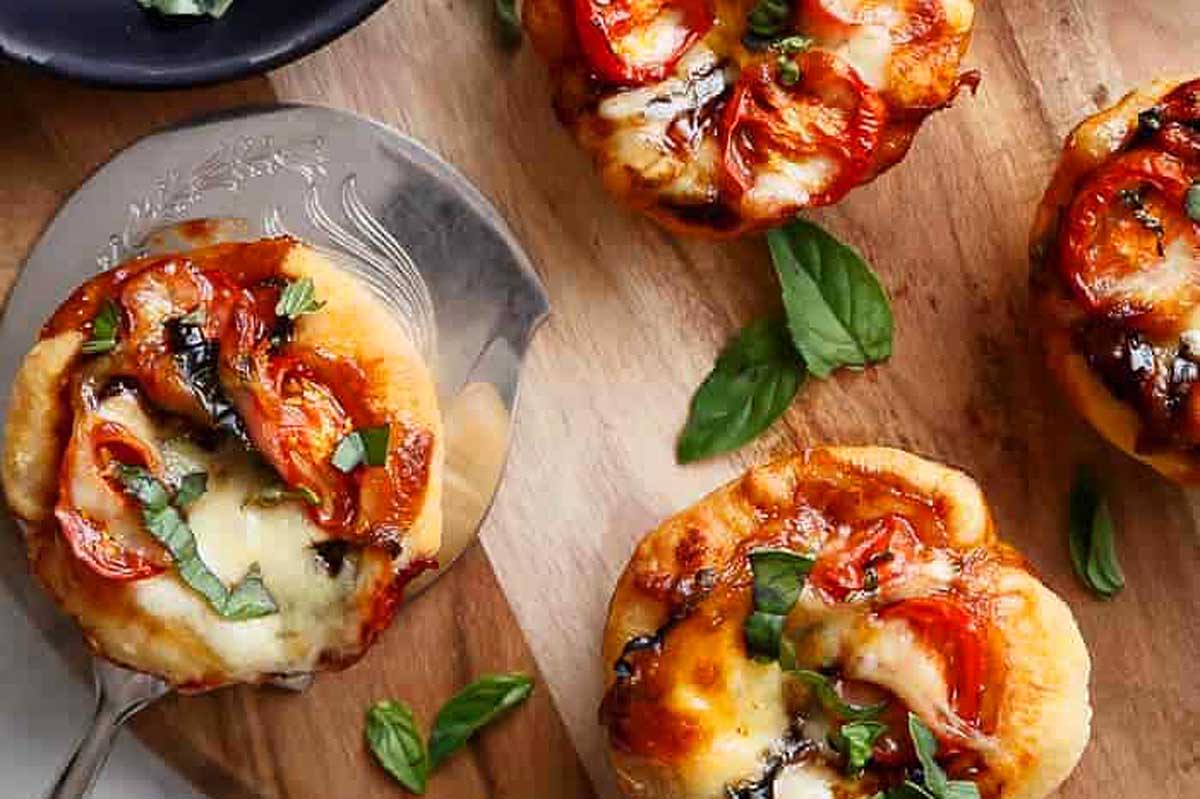 Italian appetizers - mini pizzas with tomatoes and basil on a wooden cutting board.