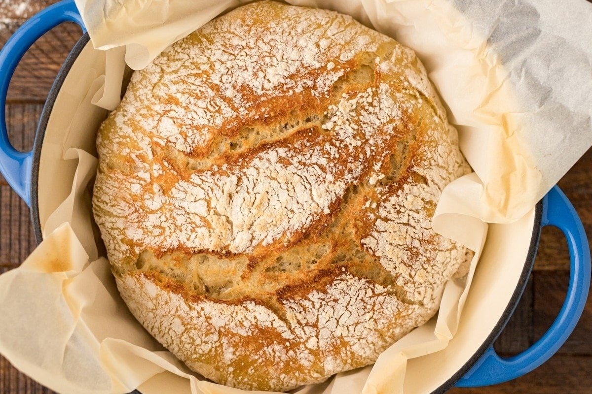 A loaf of bread from our collection of bread recipes in a blue bowl on top of a wooden table.