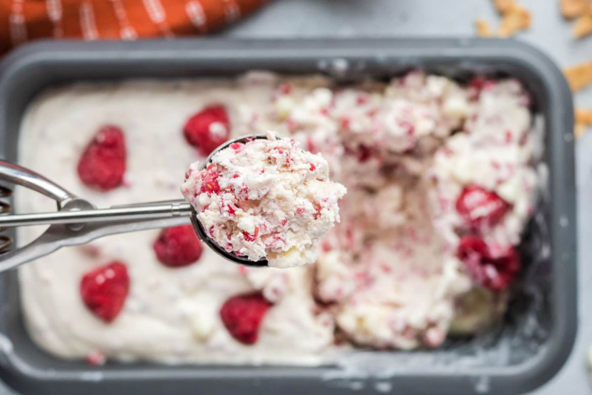 A scoop of raspberry ripple ice cream being served from a container with ice cream recipes.