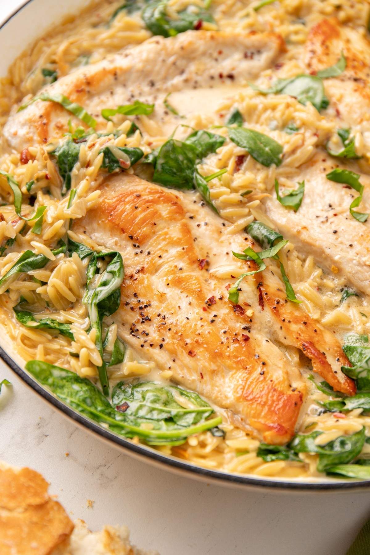 Skillet filled with cooked, seasoned Italian chicken breasts, creamy orzo pasta, and wilted spinach.