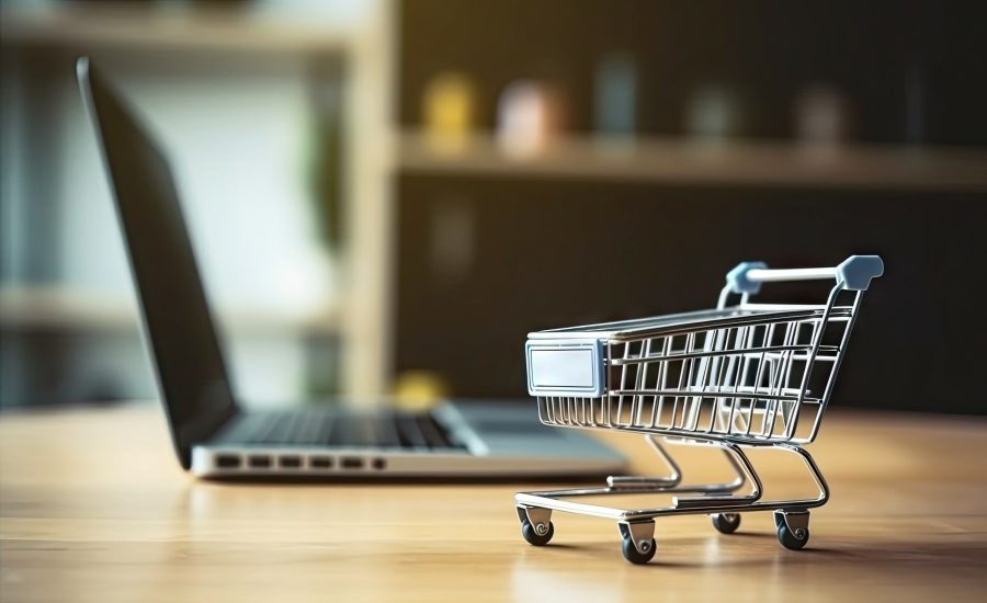 Shopping Cart Model and Laptop on Blurred Home Background. Online Business and E-Commerce Concept