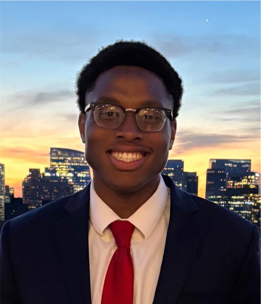 A photo of a boy with glasses and a tie smiling at the camera.