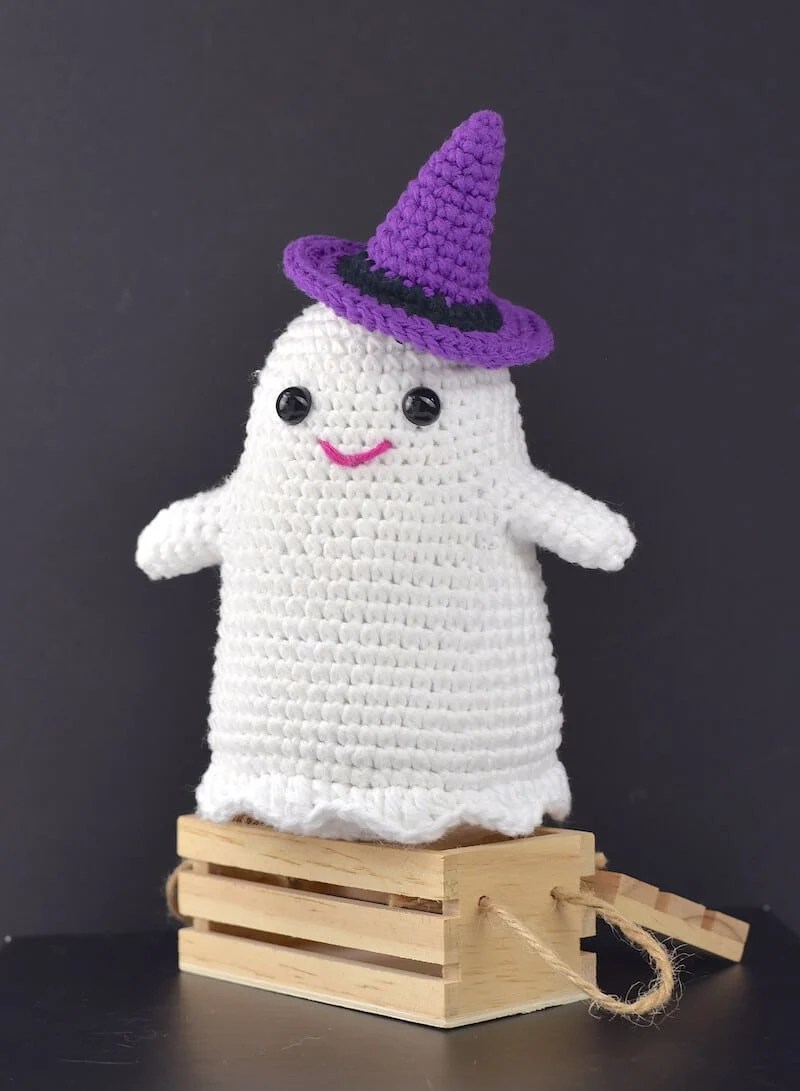 white crochet amigurumi ghost wearing a purple witches hat. 