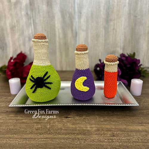 witches potion crochet patterns. Crochet amigurumi patterns for Halloween shown in green, purple, and orange on a silver tray. 