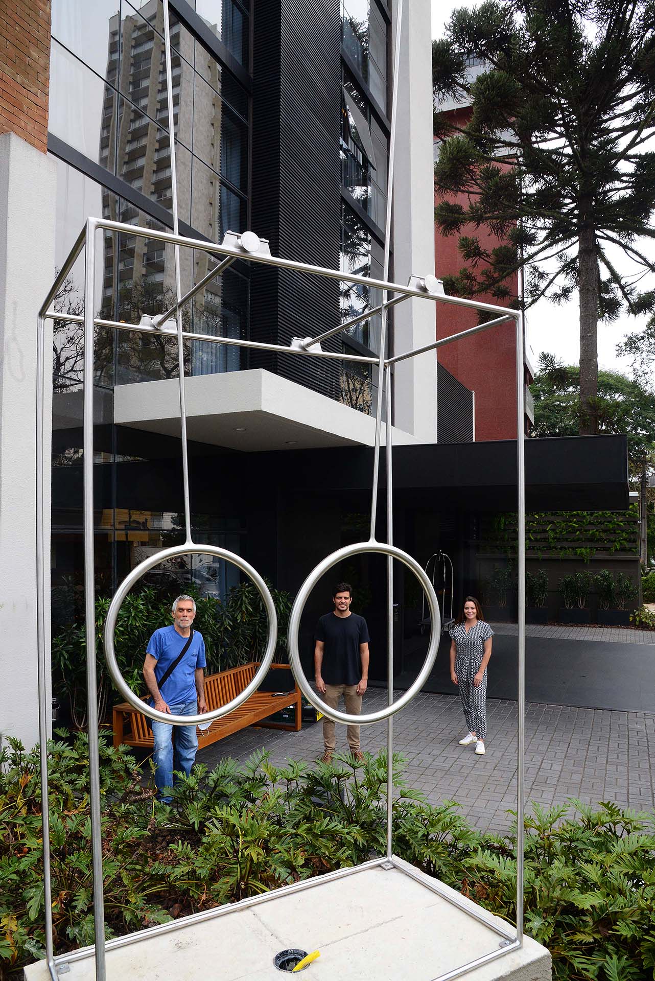 Claudio Alvarez, André e Carolina Nacli, durante a instalação da escultura "O vento e o tempo", no jardim do Hotel Nomaa, em Curitiba.