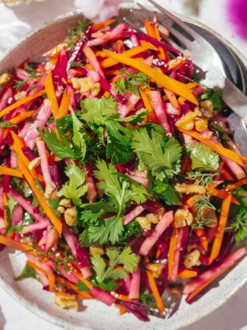 Beet and carrot salad on a plate with a fork and a knife.