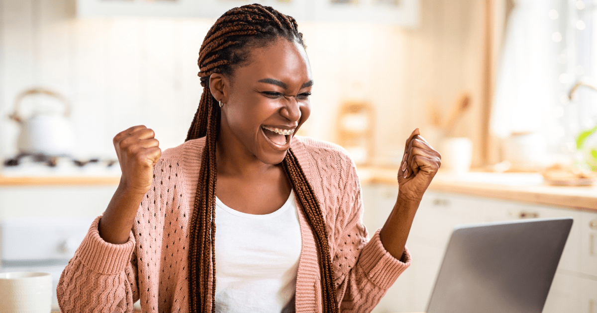 A woman celebrating at her computer, representing Write Your First Blog Post.