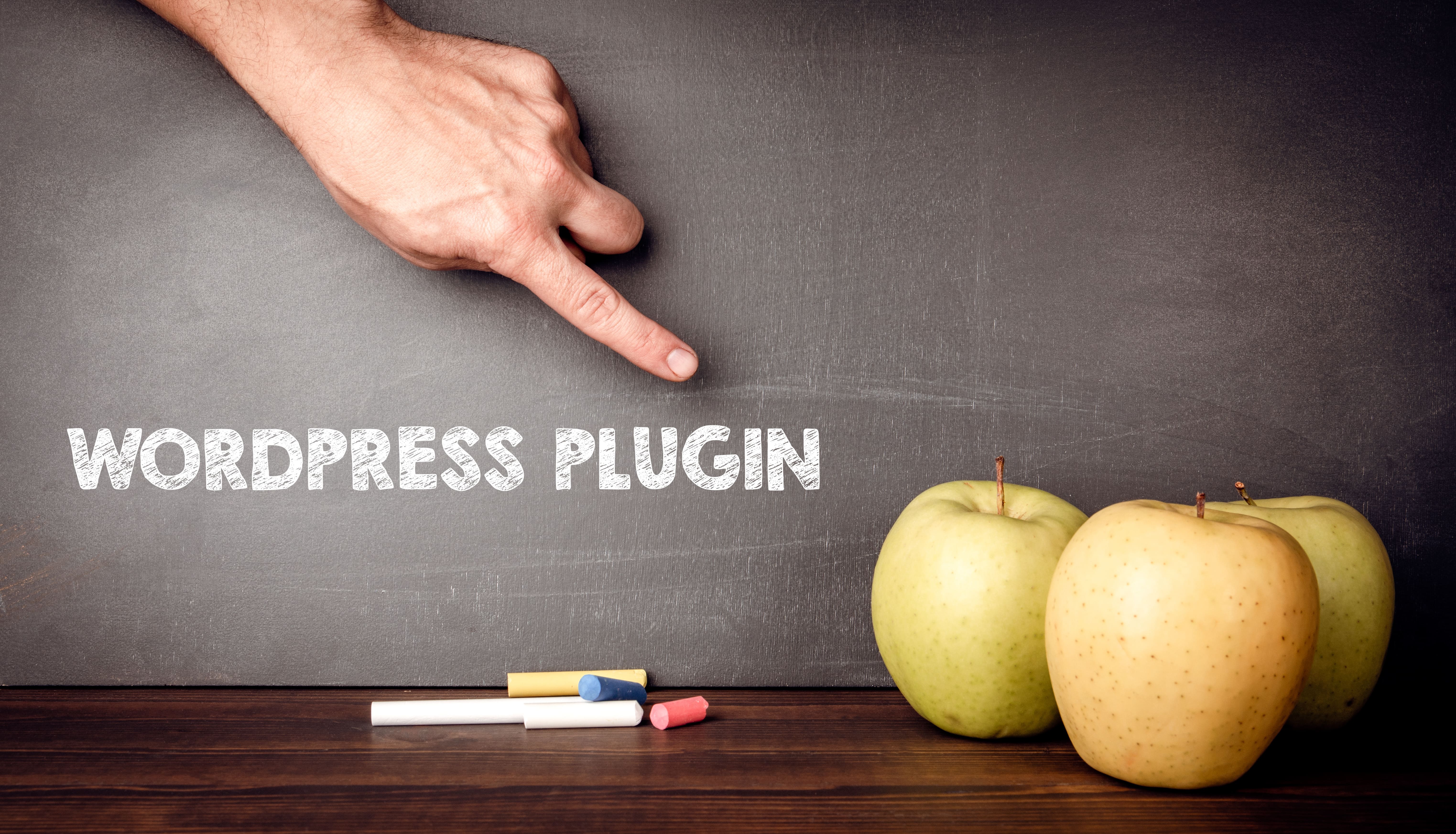 a hand pointing at a wording "wordpress plugin" with three apples on the side and colored chalk beneath the wording.
