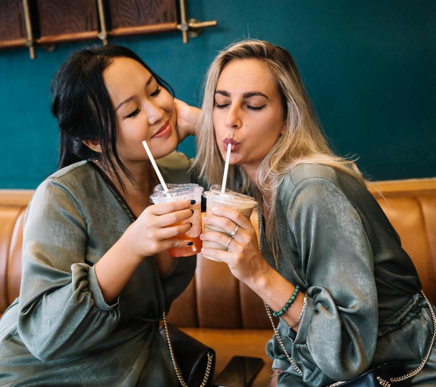 women sitting on leather couch drinking iced coffee together