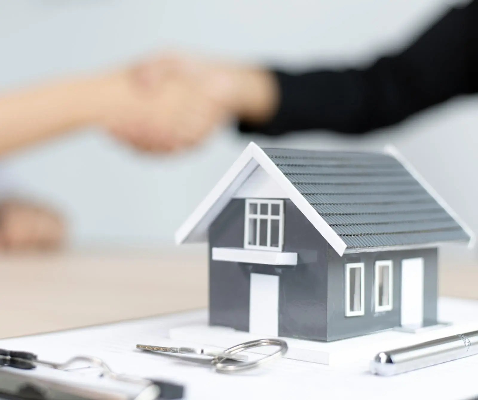 Real estate agreement with handshake, house model, keys, and contract paperwork