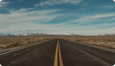 Carretera recta entre un paisaje árido y montañas al fondo.