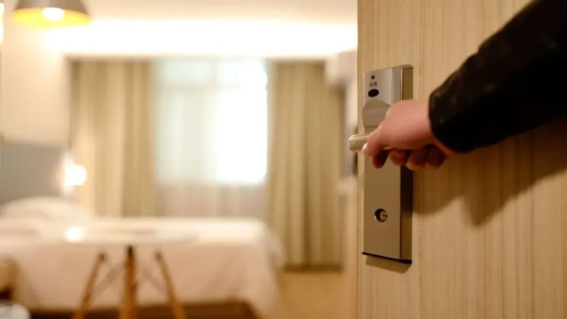 Pessoa abrindo a porta de um quarto de hotel moderno e aconchegante.