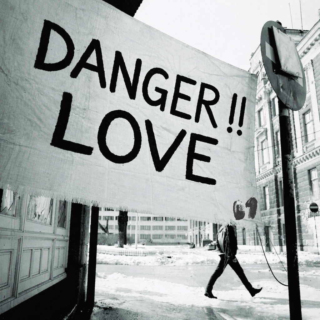 A black and white street scene with a large banner reading “DANGER!! LOVE” hanging above a person walking through a quiet urban area
