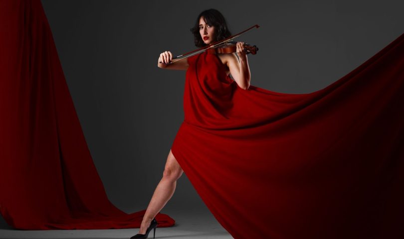 Violinist in a flowing red dress playing indoors, exuding elegance and poise.