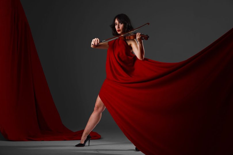 Violinist in a flowing red dress playing indoors, exuding elegance and poise.