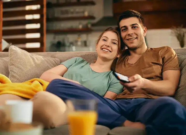 Happy young couple relaxing on sofa watching TV together.
